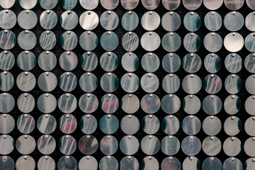 A defocused shot of repeating metallic shiny circles. A multitude of round-shaped objects fluttering in the wind. Blurred motion, selective focus, noise, grain effect.