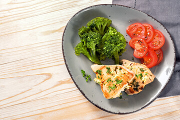 Tuna slices with broccoli and tomatoes on a gray plate and a light wooden table, healthy meal for slimming with ketogenic or low carb diet, copy space, high angle view