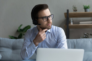 Close up confident thoughtful businessman in headphones and glasses looking in distance, touching...