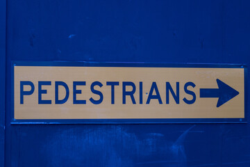 Blue Pedestrians sign on wall pointing with arrow which way to go