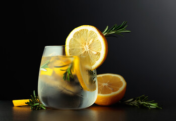 Cocktail gin-tonic with lemon slices and twigs of rosemary on a black background.