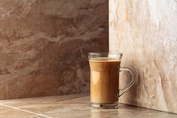 Glass cup of coffee latte on a beige ceramic table.