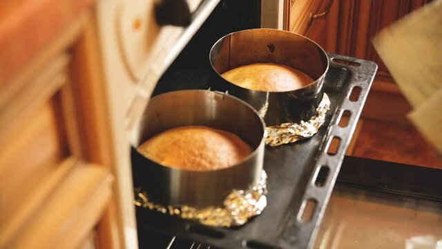 A woman pastry chef checks that the cake layers are ready by taking them out of the oven.