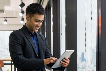 Young businessman executive in suit and smiling using tablet on window with city building background.