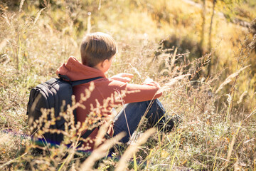 Autumn portrait of teenager boy sitting on grass. Young man with backpack resting relaxing,...