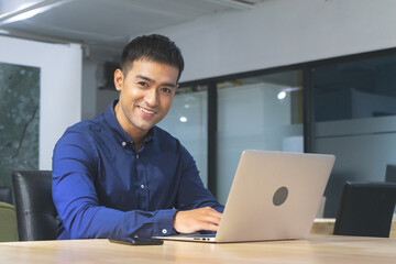 Young asian businessman executive smiling using laptop sitting at work desk in office building.