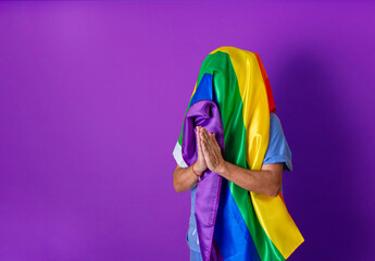 Fototapeta premium Unrecognizable person with LGBT flag covering his head. Gay pride concept. Purple background with copy space.