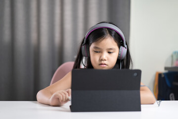 asian child student or kid girl learning art drawing or write on computer tablet by touch pen on touch screen and wearing headset for video call or person learn from home school by study online class