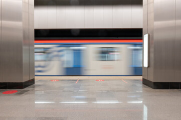 Underground station, gray walls, the train rushes by. Nobody, motion blur. City life. Background for travel design, construction, business.