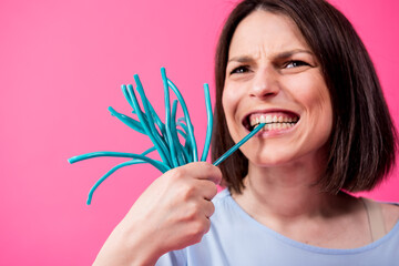Young woman with sensitive teeth eating sweet candies on color background