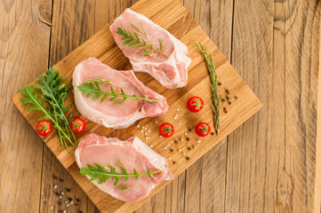 three perfect pieces of fresh pork on a cutting kitchen board with arugula leaves and tomato. top view.