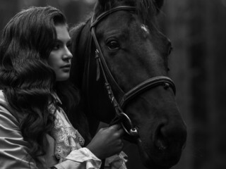 Fototapeta na wymiar A young beautiful brunette rider next to a black mare in full ammunition,