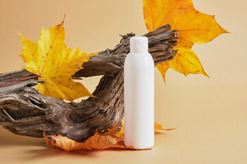 white mock up bottle without label for cosmetics on the background of driftwood and autumn leaves