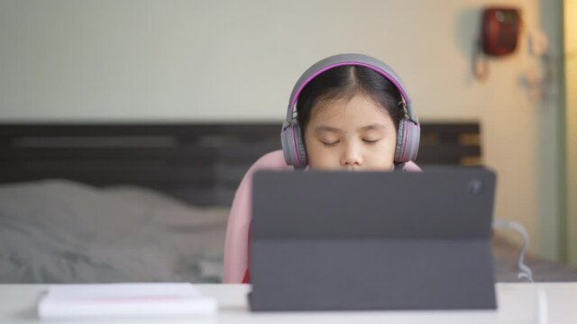 asian child learning smile on computer tablet or kid girl student back to school and wearing headset for video call studying or person enjoy learn from home by study online listening class in bedroom