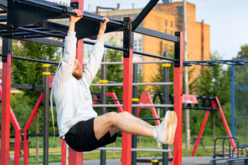 Fototapeta premium A man performs a leg raise on the bar in the morning on the sports field