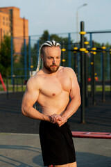 Obraz premium In the morning at sunrise, a man with an interesting braid hairstyle poses like a bodybuilder with a naked torso