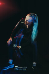 A handsome man with an interesting hairstyle from braids on a black background shakes his biceps with dumbbells 5 kilograms, shooting with mixed light