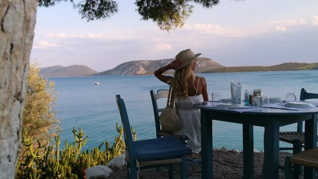 Beautiful girl tourist sitting at summer cafe with sea and mountains on background at Ermioni, Greece