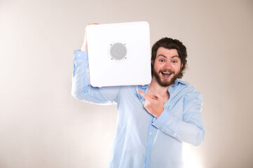 Young attractive man  holding white portable bluetooth speaker on shoulder on gray background