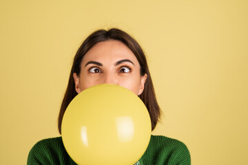 Young woman in green warm sweater happy funny playful blowing air balloon