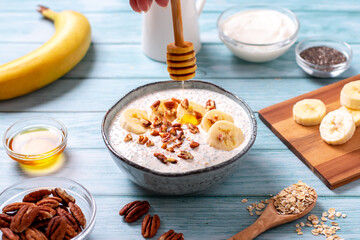 Banana and pecan nuts overnight oatmeal with chia seeds in bowl, rich in protein breakfast or snack
