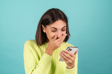 Young woman in light green sweater with mobile phone shocked laugh funny surprised read joke