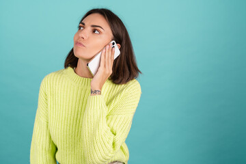 Young woman in light green sweater with mobile phone having conversation listen audio message bored unhappy tired