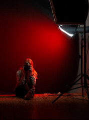 woman sitting in a photo studio with a camera against a red light background