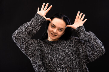 woman with long hair wearing gray sweater on a black background gesticulating with her hands