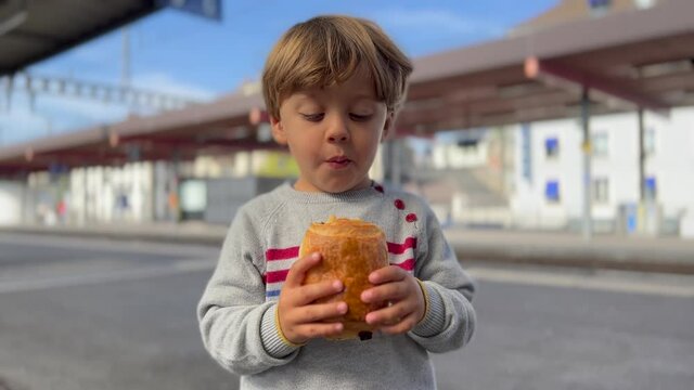 Little boy eating bread made of chocolate at train platform