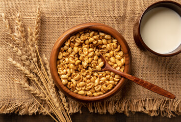 Wheat flakes cereal breakfast in wooden bowl with dry spikelets on the rustic background. Selective focus.