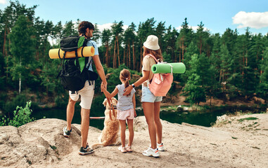 A family with backpacks and a labrador dog stands on a rocky peak, looking at the river and the...