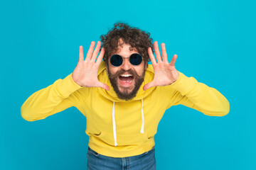 Naklejka premium excited young guy in yellow hoodie making funny faces and laughing