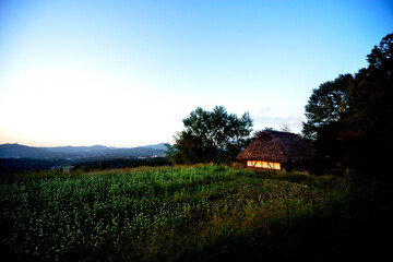 夕暮れの蕎麦畑と茅葺の家