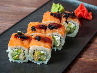 side view of juicy delicious rolls decorated with caviar. Japanese cuisine, black plate, close up