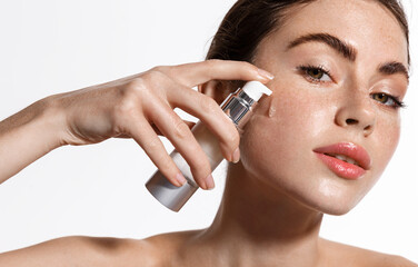 Young woman with clean glowing skin, holding bottle of skincare product, spf essential oil, facial...