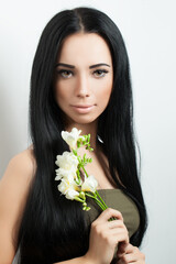 Young brunette woman with long healthy straight hair holding flowers