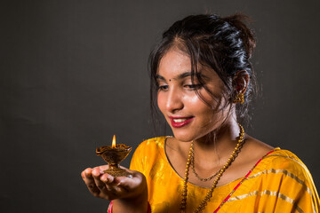 Beautiful Girl in Indian saree holding diwali diya(oil lamp) on gray background. Happy Diwali....