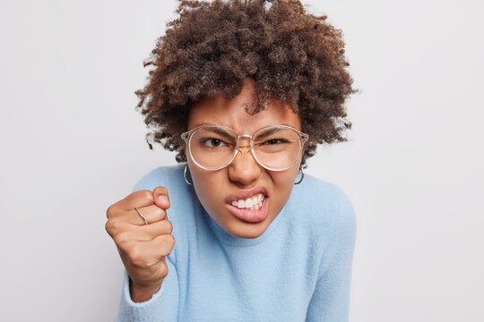 Angry irritated Afro American woman clenches fist and teeth expresses negative emotions being fed up of something dressed casually isolated over white background. People and reactions concept