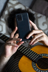 Top view of a man with guitar lying on a sofa and using a phone.