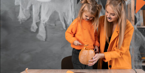 Halloween portrait of mom and daughter girl takes out pumpkin seeds with a spoon to prepare a jack-o-lantern for the autumn holiday.Place for text