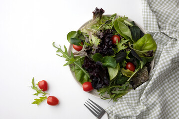 Healthy vegetable salad of fresh cherry tomato and green leaves mix on plate. Top view. White background. 