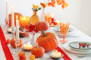 autumn table setting with burning candles and pumpkins