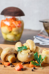 Marinated white mushrooms on a cutting board on a light background with carrots and herbs