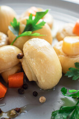 Canned porcini mushrooms in a close-up in a gray plate with carrots and herbs