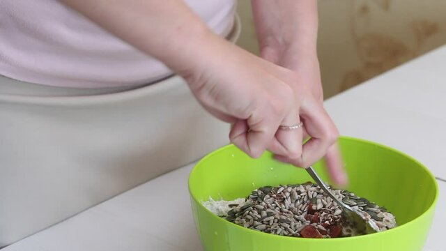 Making bread from green buckwheat. A woman adds flax, sunflower and pumpkin seeds to the green buckwheat dough. Begins to stir the dough with a spoon. Close-up shot.