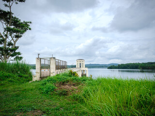 Fototapeta na wymiar Wide angle view of Caliraya dam's water intake tower, tranquil lake, and grassy shore.