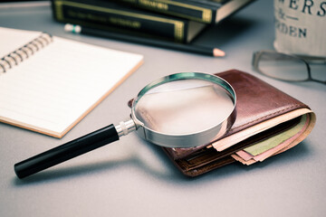 Closeup magnifying glass on the leather wallet with banknotes on the desk, check the financial...