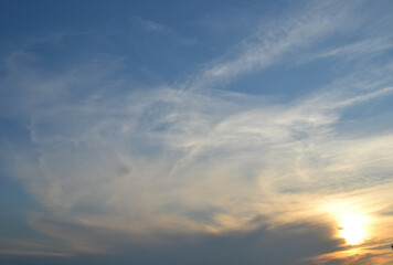 Sun behind clouds on sunset sky.