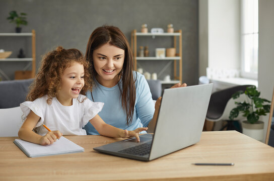 Excited smiling mother and little child with pencil sitting at table at home, looking at screen of new laptop computer, learning online, having fun interesting class, doing homework with private tutor